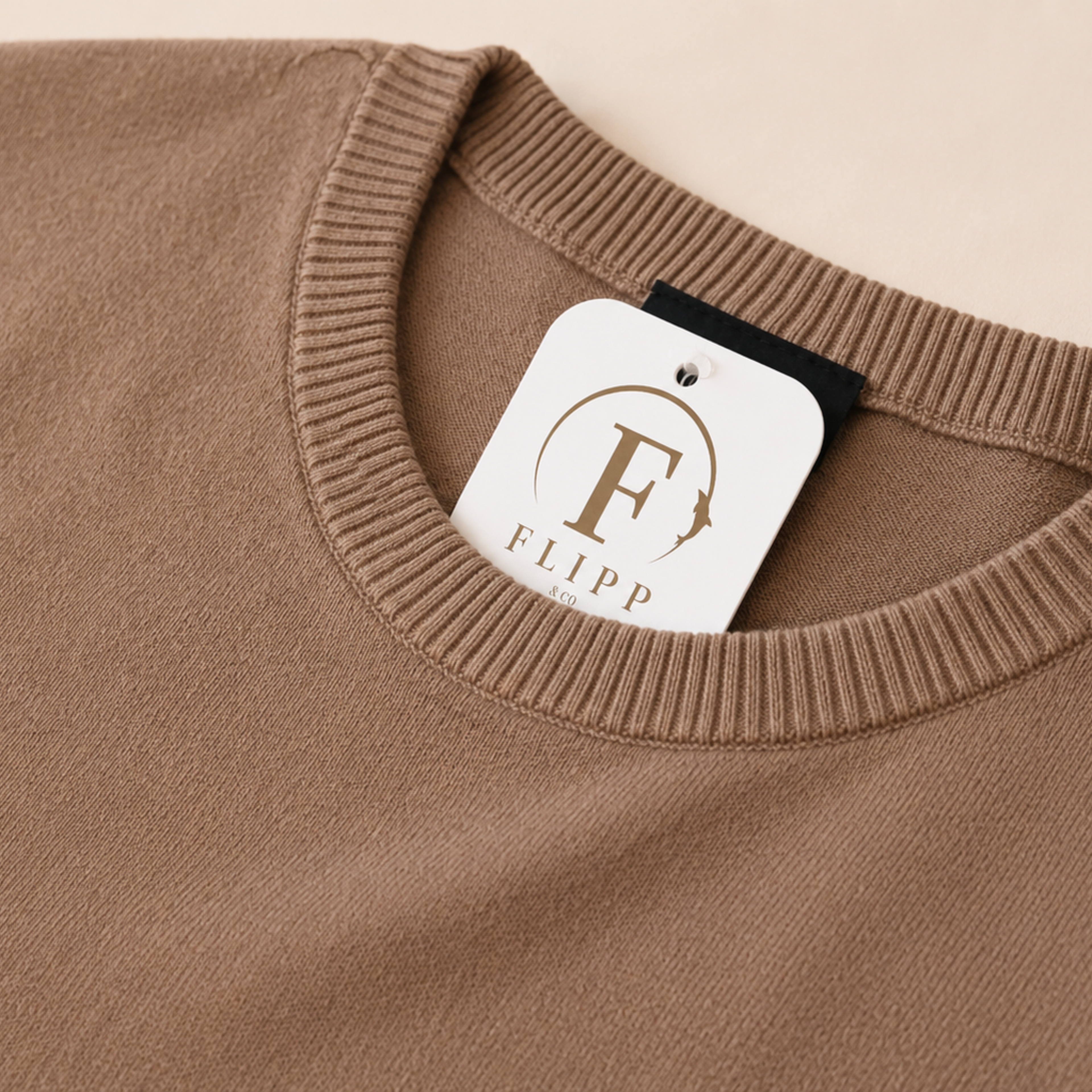 Close-up of a ribbed crewneck sweater in a warm taupe-brown color, with a white FLIPP brand hangtag visible at the collar.