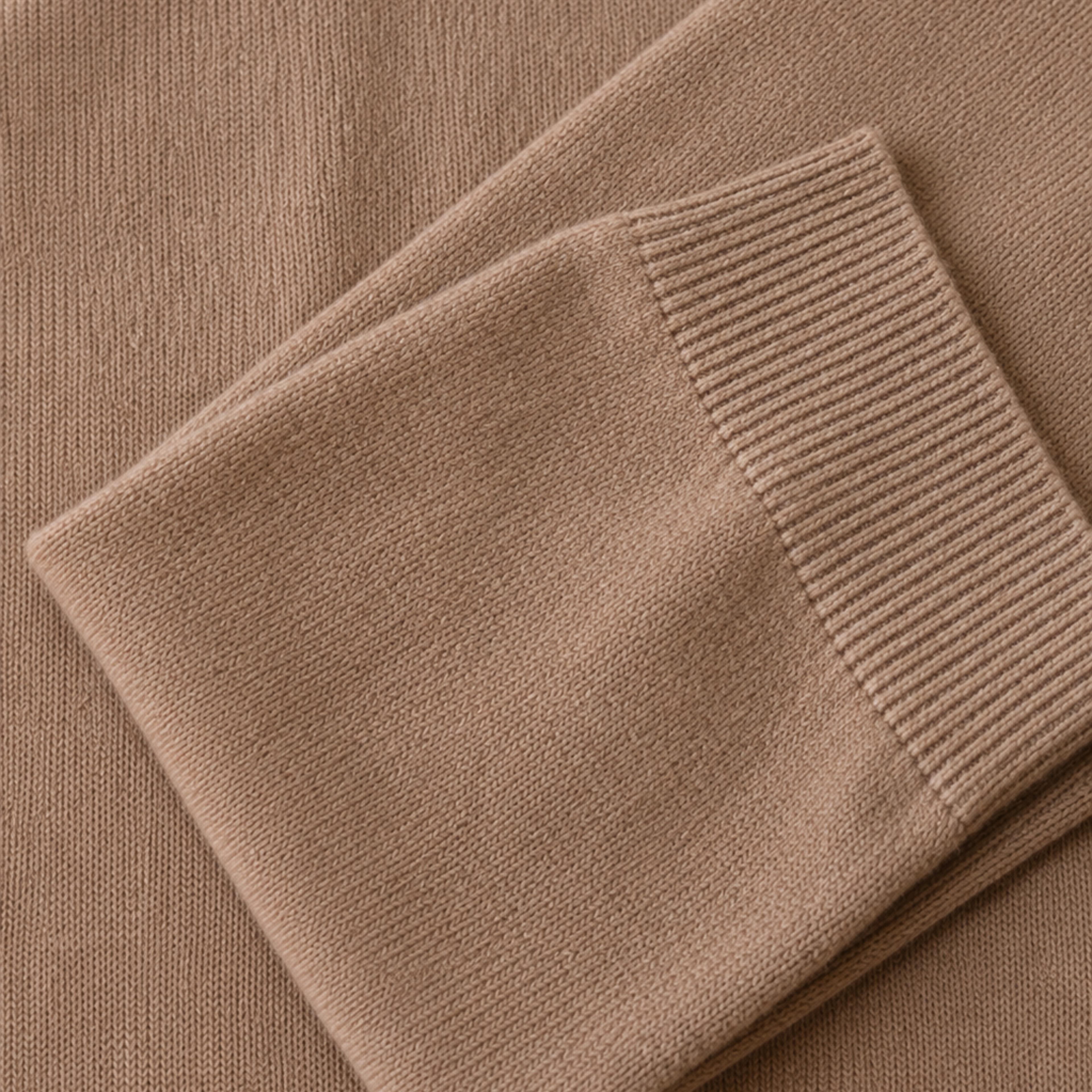 Close-up of a folded knit garment in a warm taupe-brown color, showing the ribbed cuff and fine knit texture.