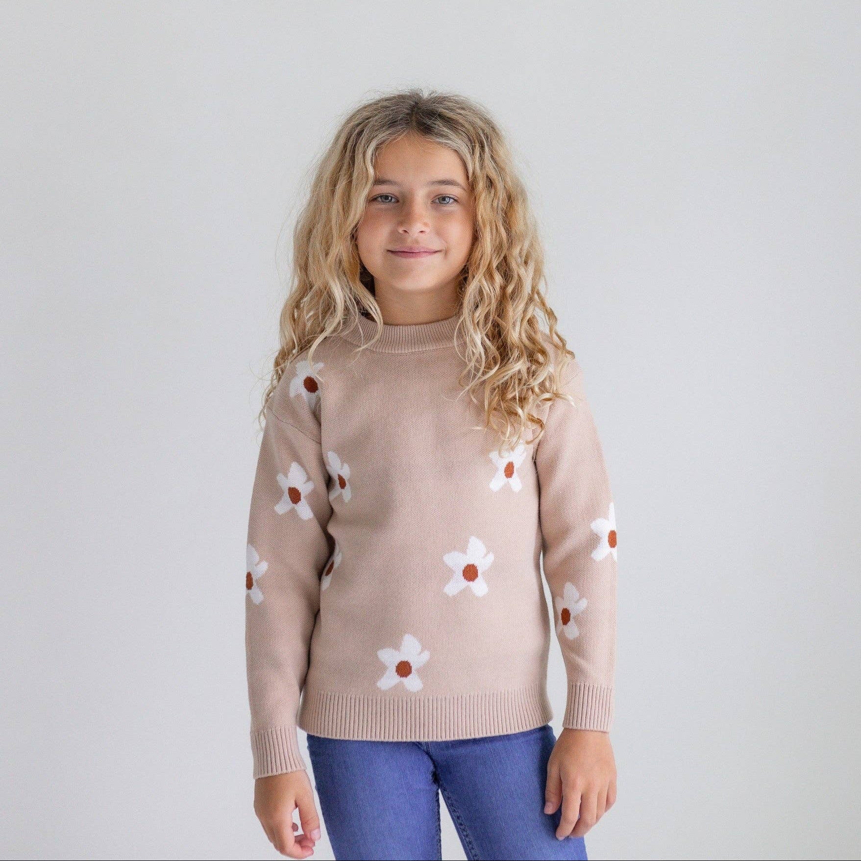 Young girl wearing a beige sweater with floral patterns on a plain background