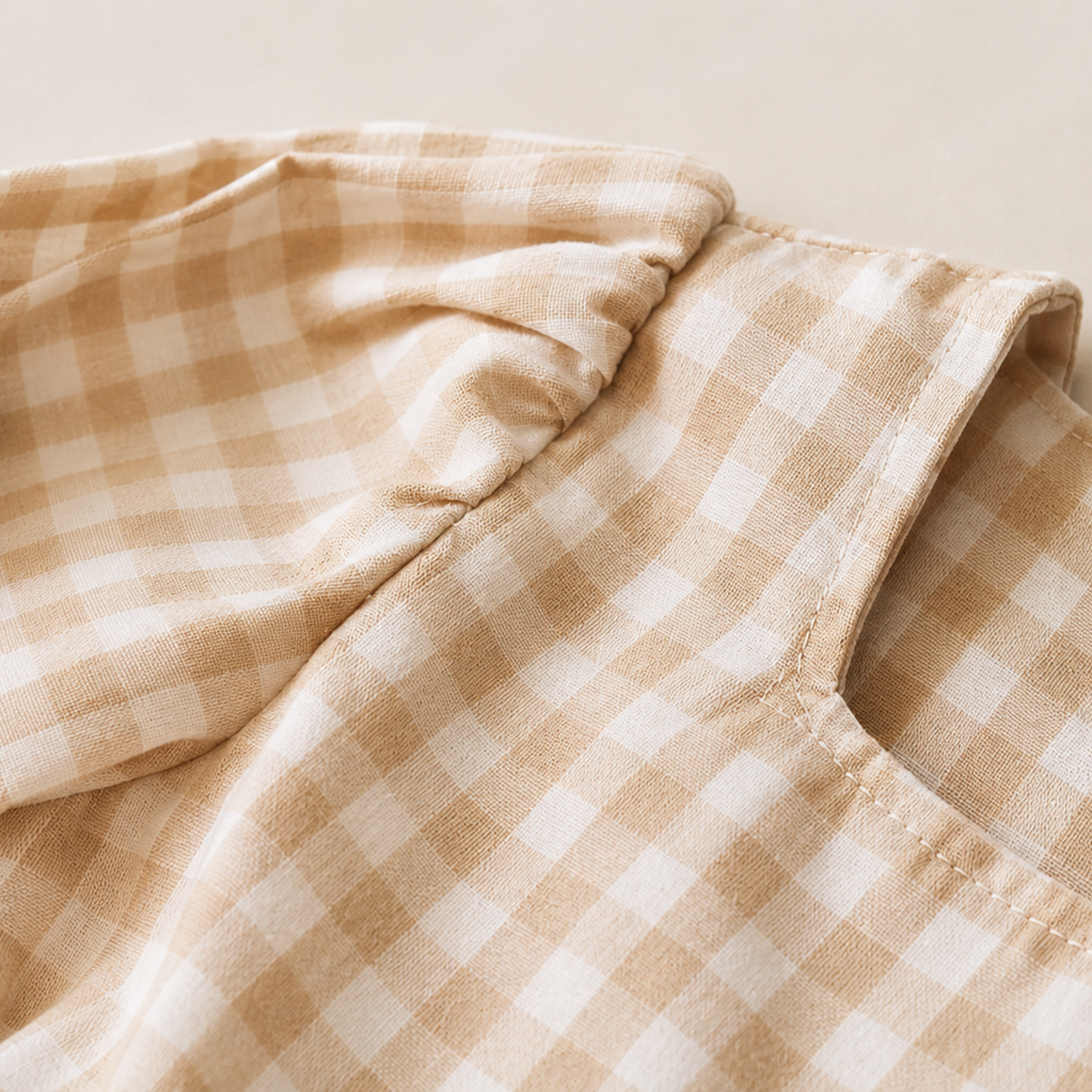Close-up of a beige and white gingham fabric garment, showing the texture and checkered pattern.