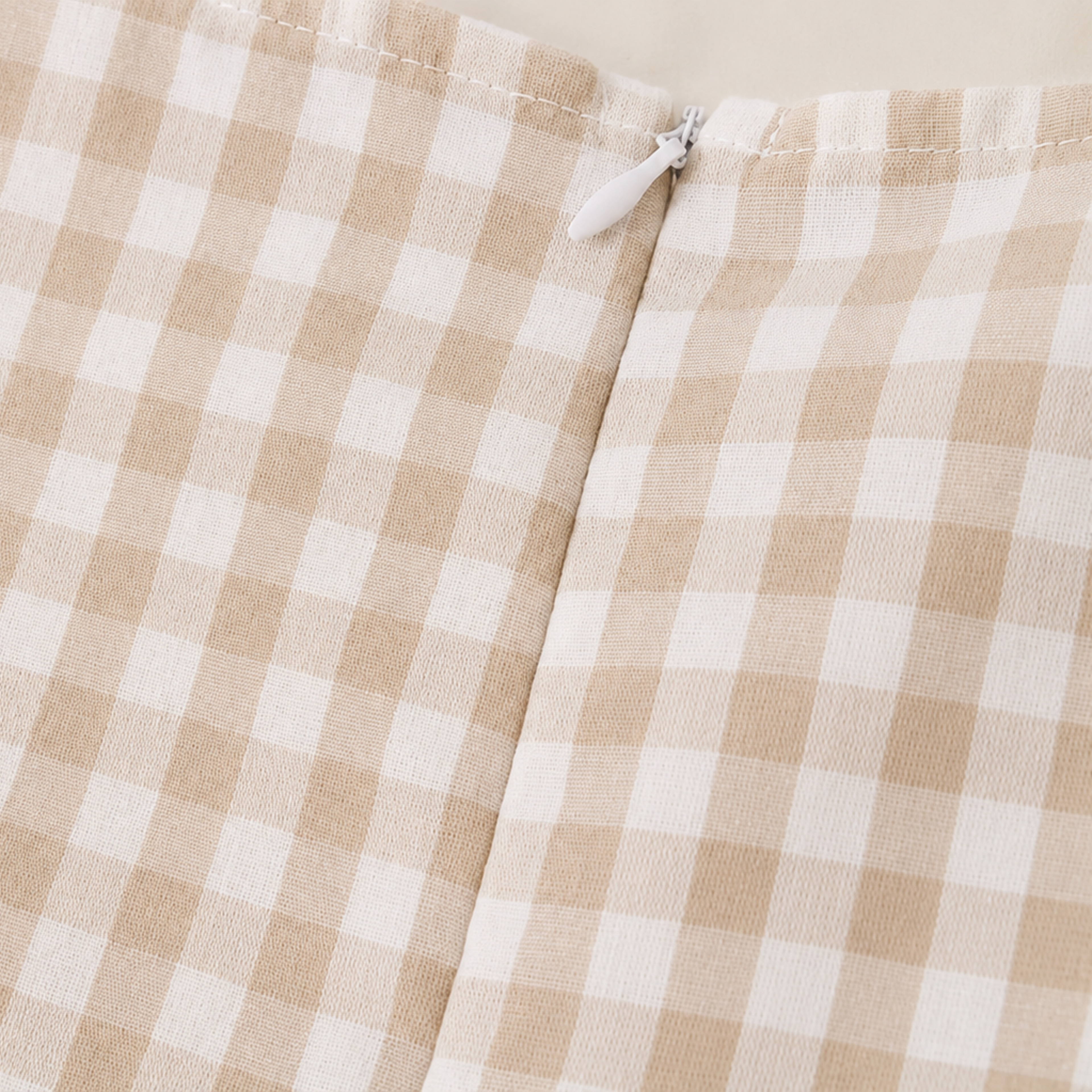 Close-up of a beige and off-white gingham check fabric with a small white zipper pull visible at the top center.