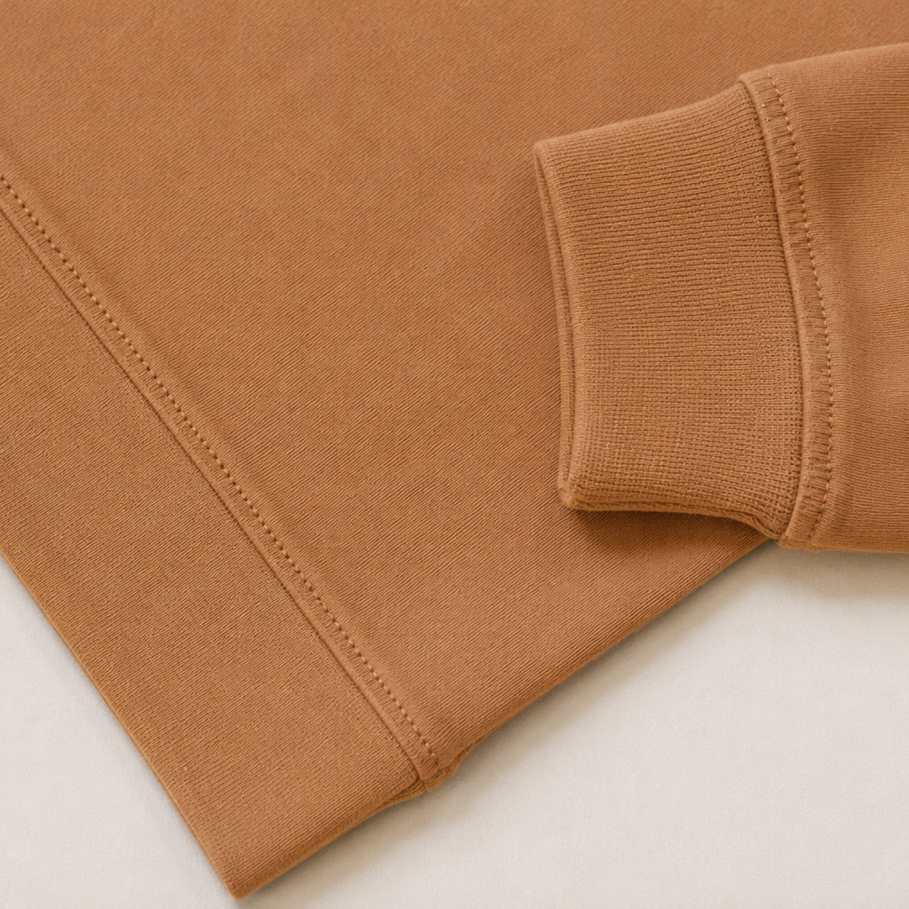 Close-up of a camel brown ribbed knit fabric, showing the texture and a folded cuff detail on a light off-white background.