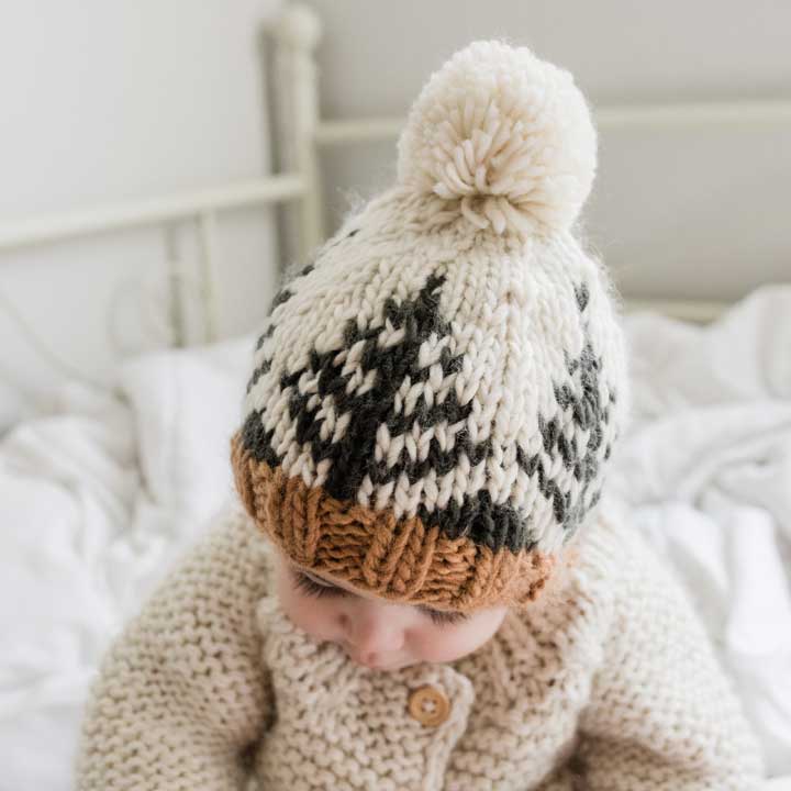 Baby wearing a knitted hat with a pom-pom on a bed