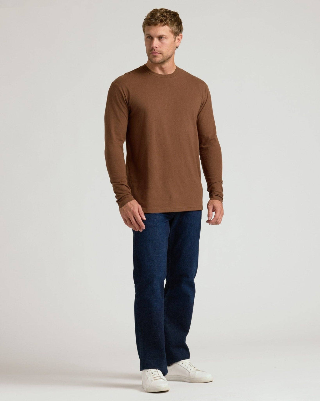 Man wearing a brown long-sleeve shirt and blue jeans on a white background