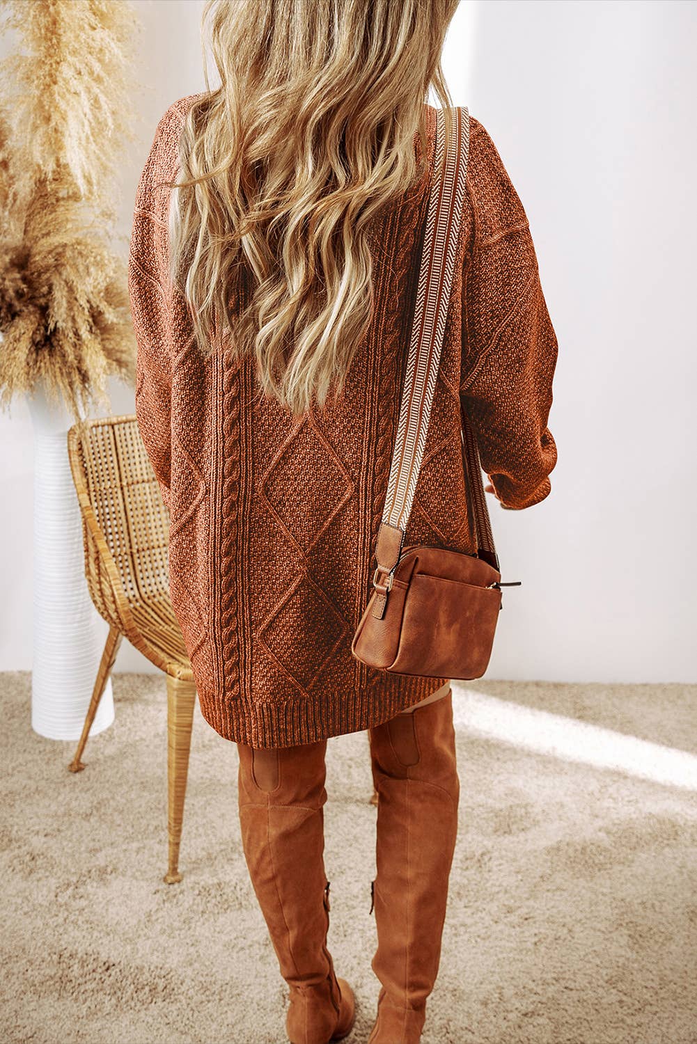 Person wearing a brown knitted cardigan and matching over-the-knee boots, holding a brown leather bag.