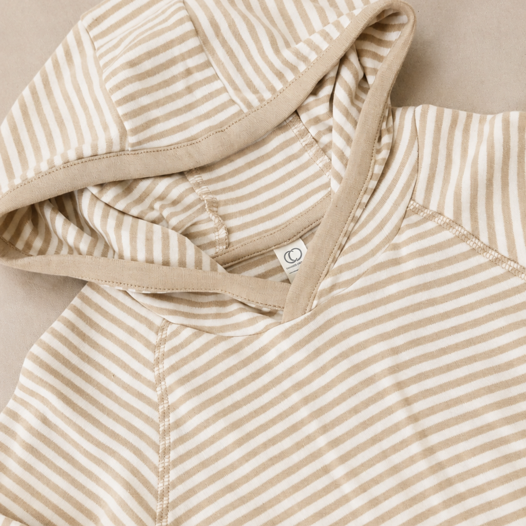 Close-up of a beige and off-white striped hooded sweatshirt, showing the striped fabric, hood lining, and drawstrings on a neutral background.