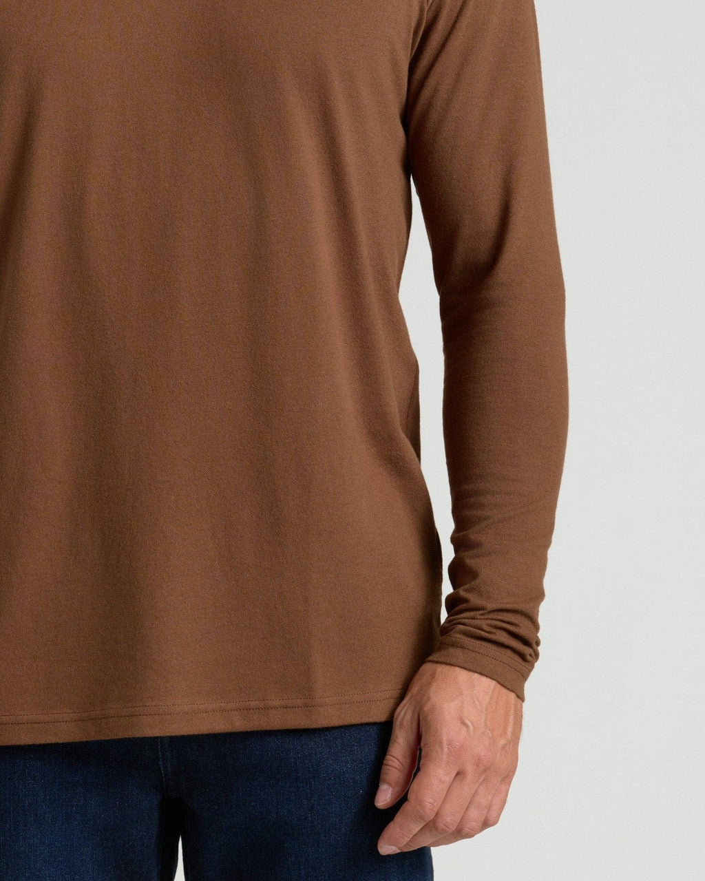 A close-up of a person wearing a brown long-sleeve ribbed knit top with dark blue jeans, shown against a light gray background.