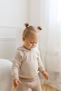 Child wearing a striped shirt and light-colored pants in a softly lit room.