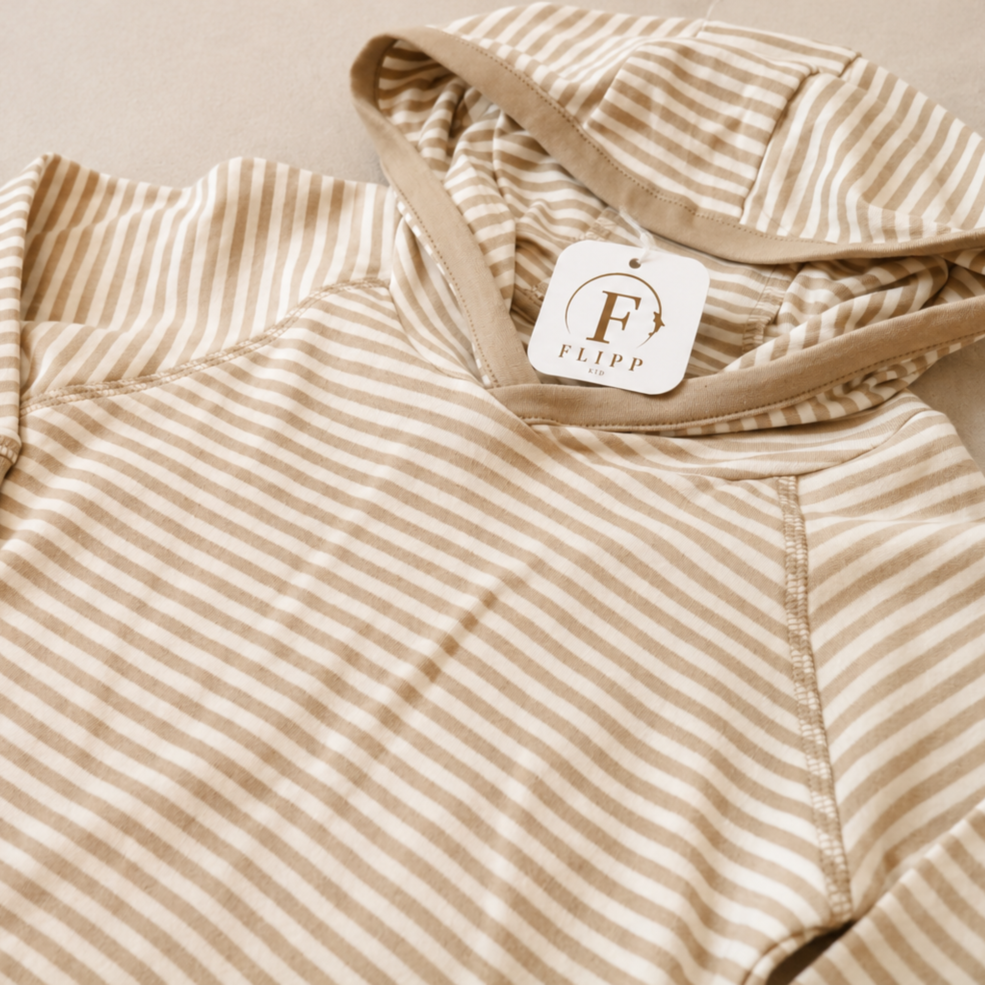 A close-up of a beige and cream striped hooded sweatshirt with a visible white brand tag reading 'FLIPP & CO'.