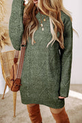 Person wearing a green cable knit sweater with a brown bag and knee-high boots indoors.