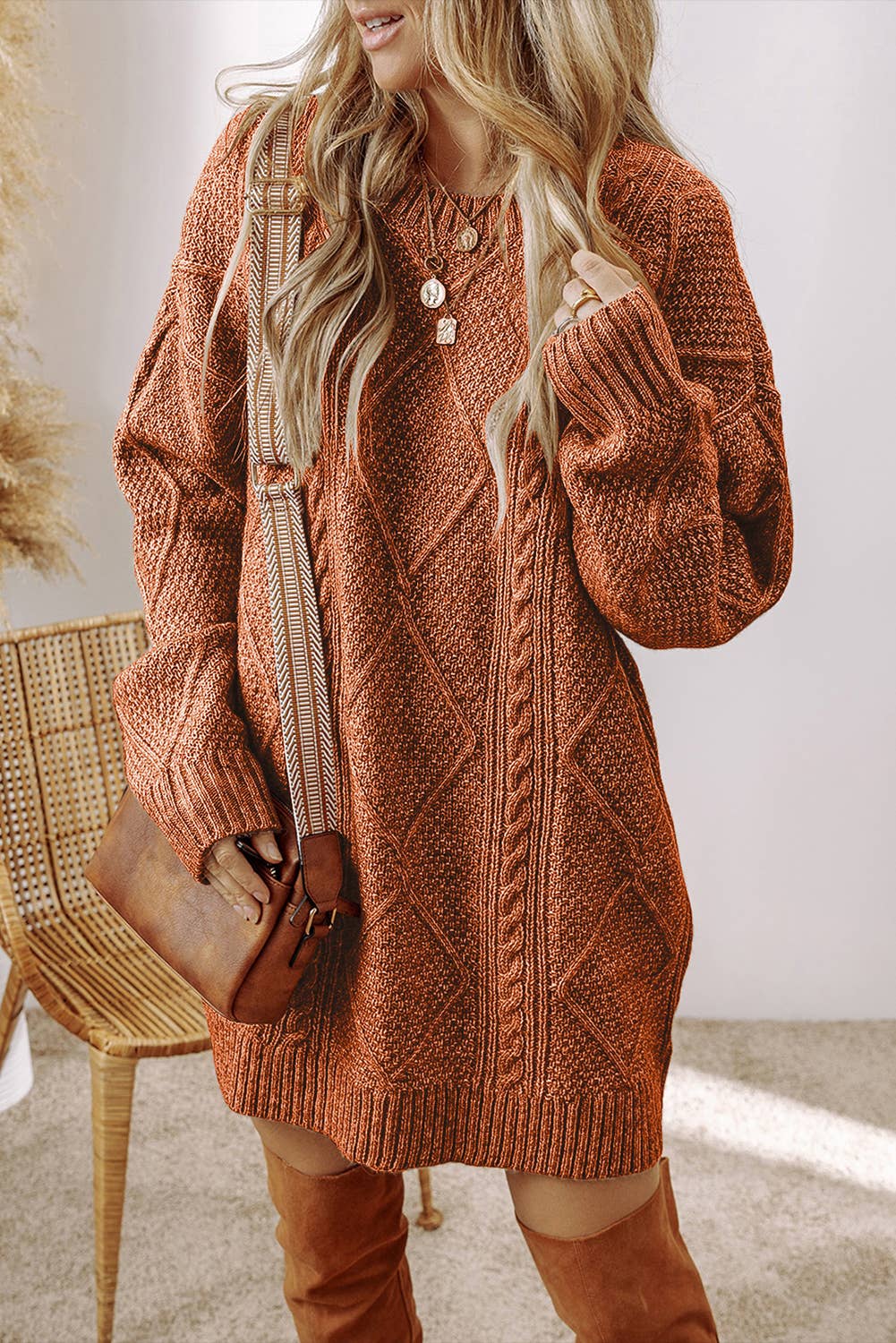 Person wearing a brown knitted sweater dress with over-the-knee boots, holding a brown bag.