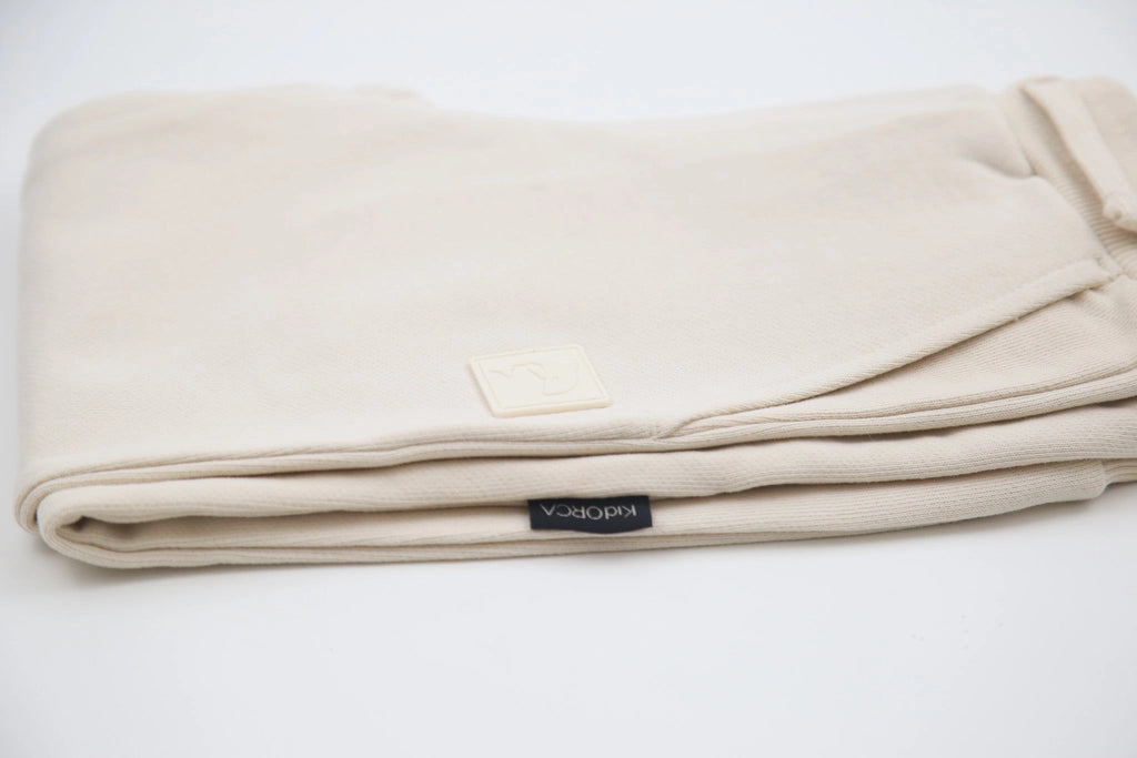 A folded cream-colored cotton blanket with a small square brand patch and a black fabric brand tag reading 'KIDORCA', shown on a clean white background.