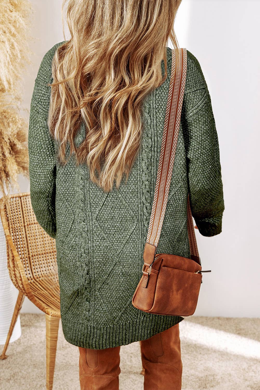 Person wearing a green knitted sweater and brown boots with a brown bag, standing indoors.