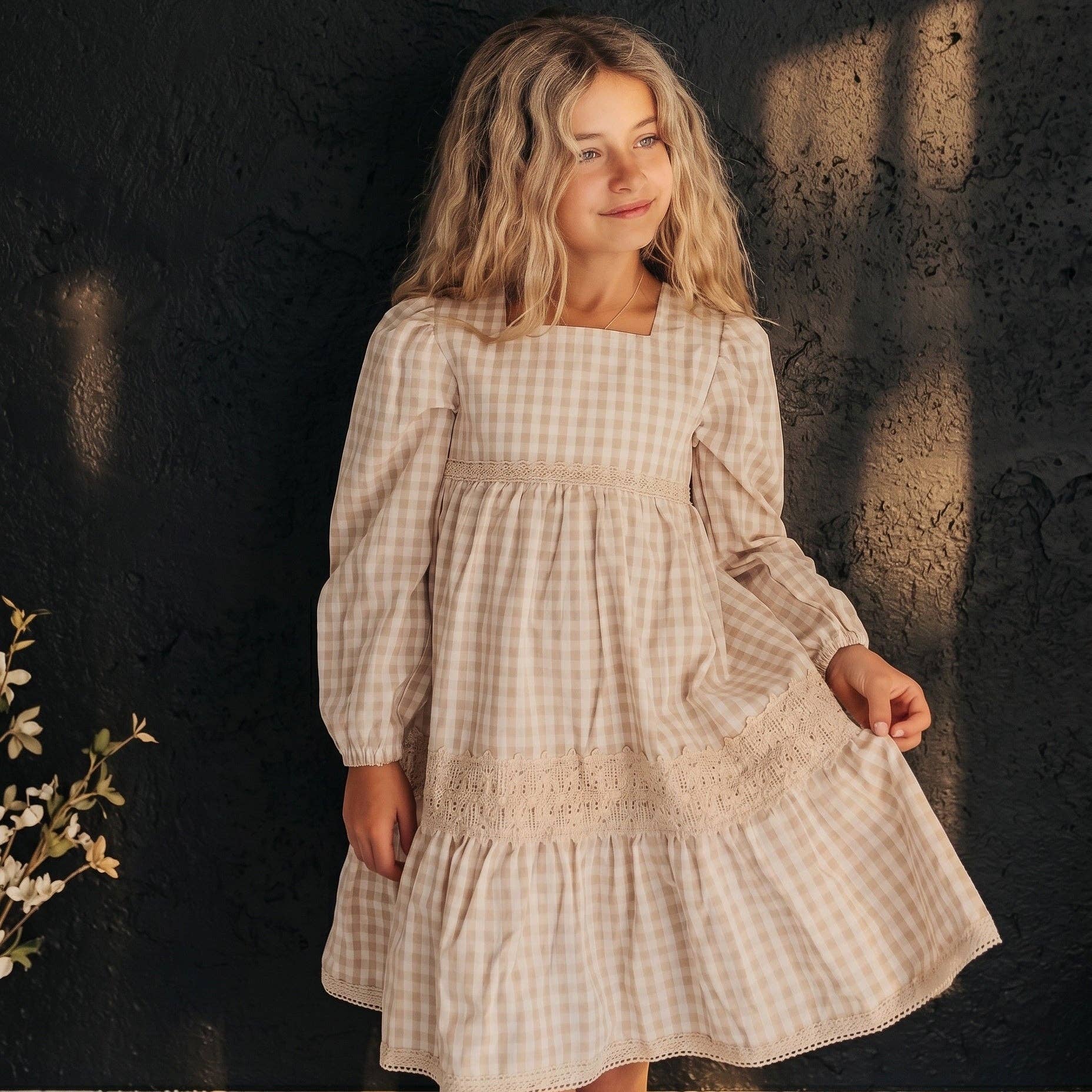 Young girl wearing a checkered dress against a dark textured wall.