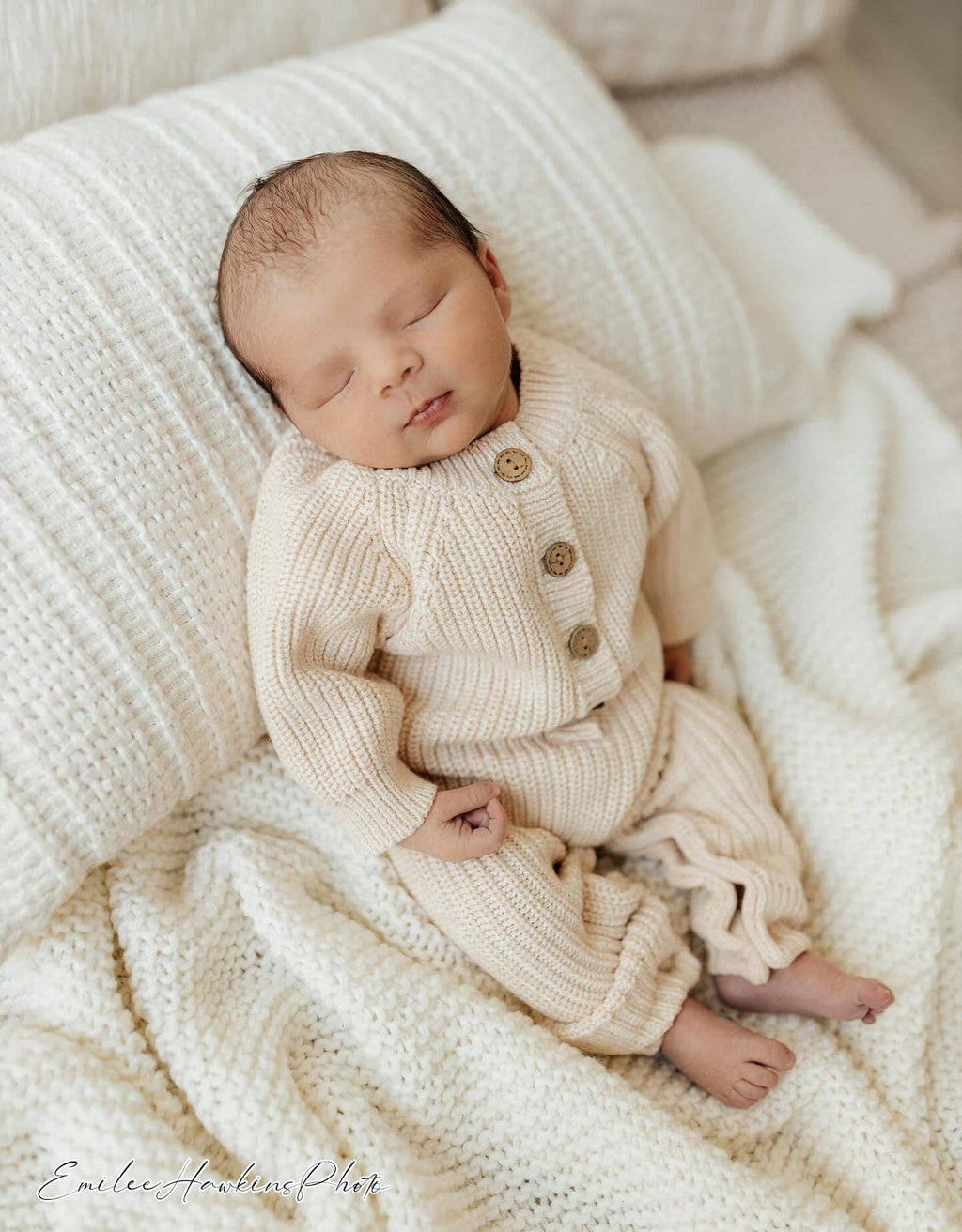 Newborn baby in a cream knitted outfit lying on soft bedding
