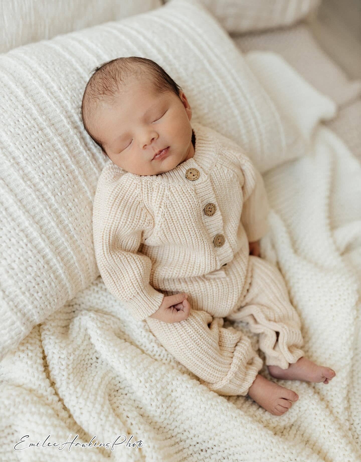 Newborn baby in a cream knitted outfit lying on soft bedding