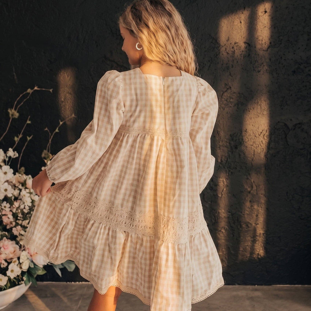 Woman in a checkered dress standing next to a floral arrangement against a textured wall.