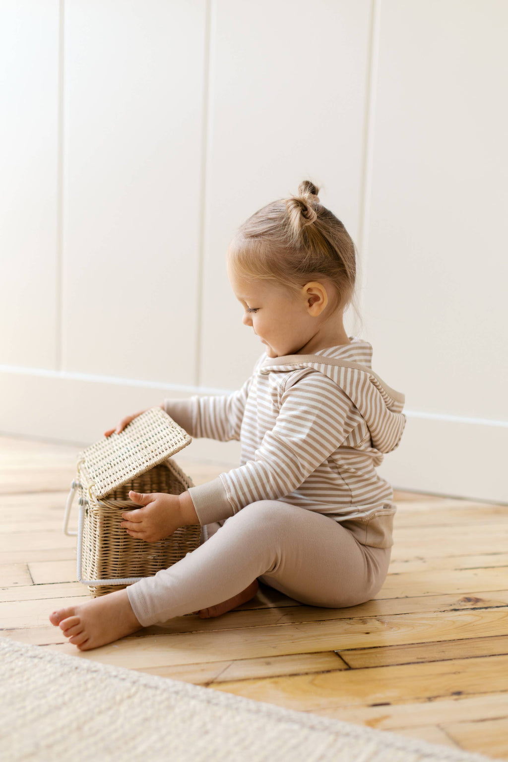 Child sitting on a wooden floor with a wicker basket