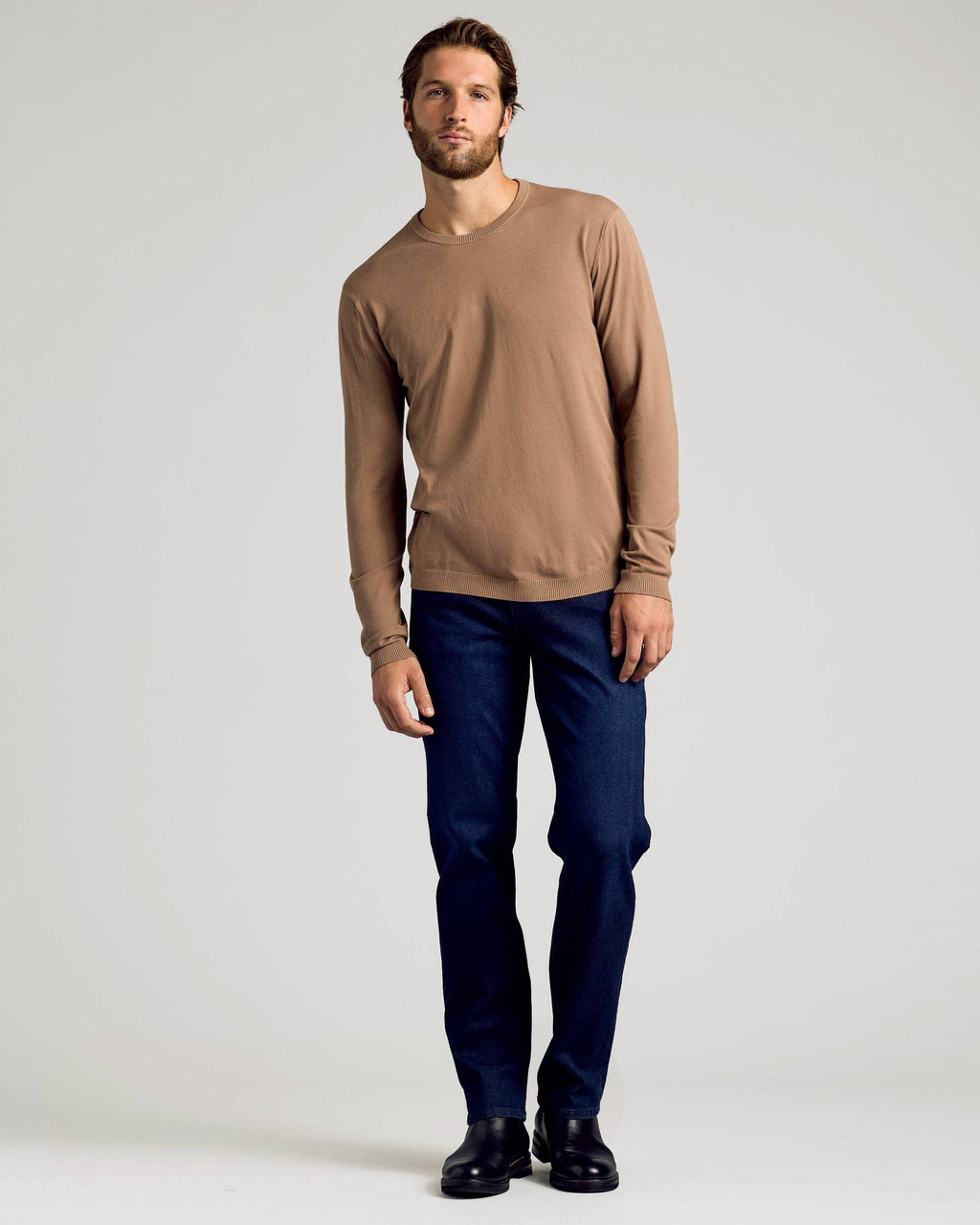 Man wearing a brown sweater and blue jeans on a white background