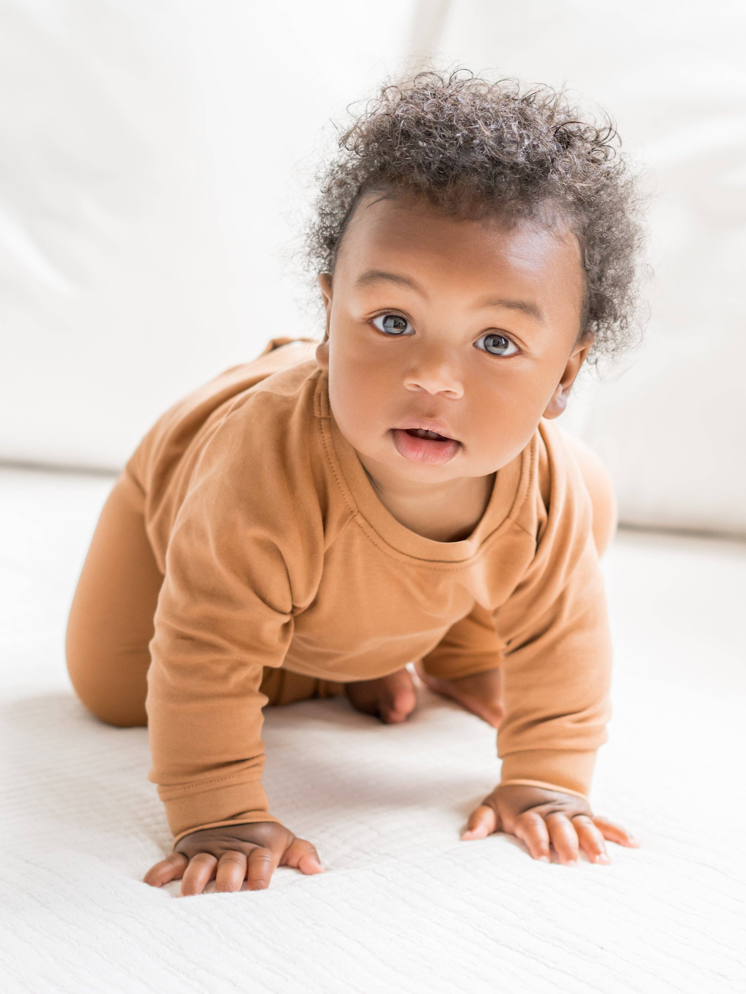 Baby in a brown onesie crawling on a white surface